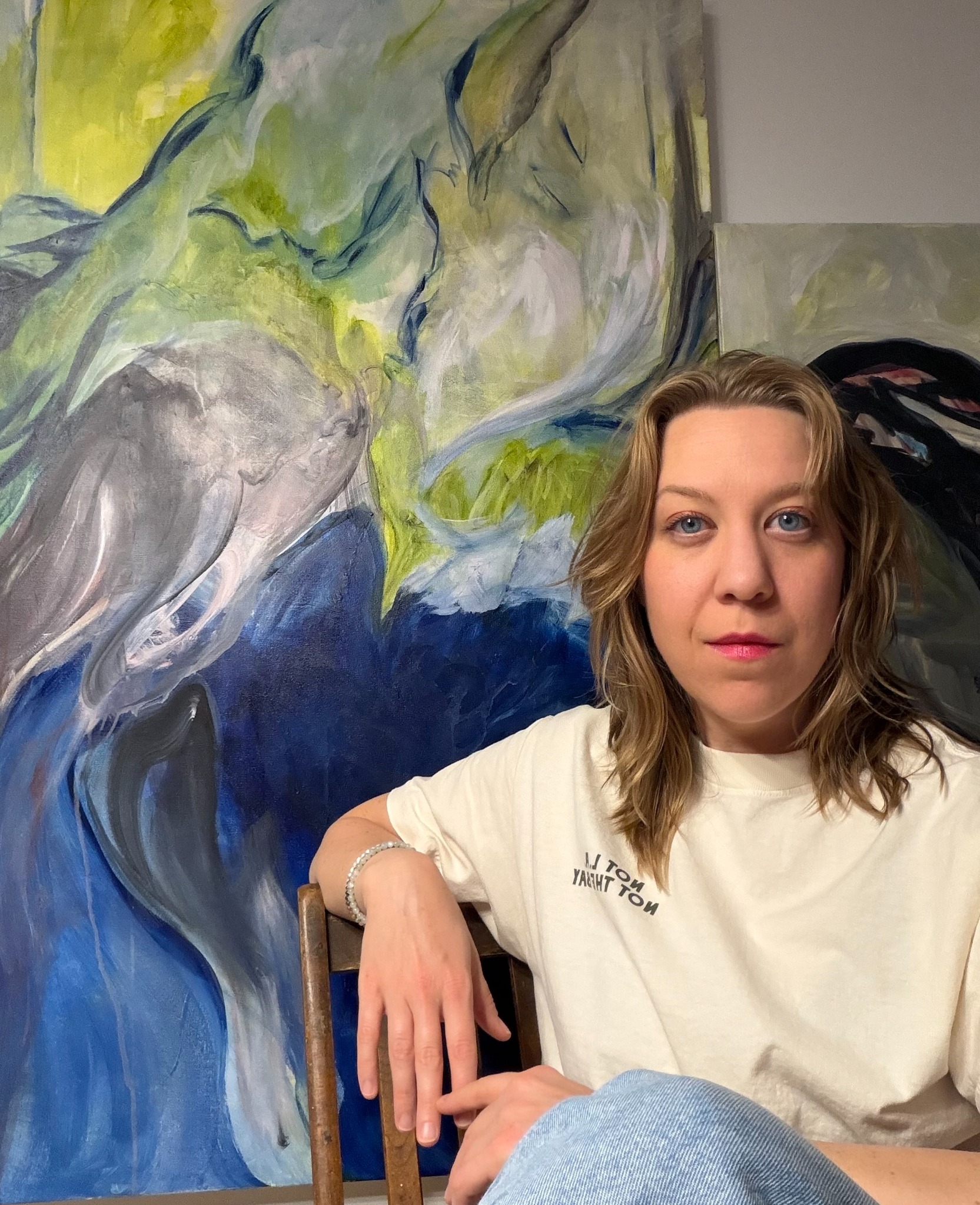 Mae Sevick seated in her studio in front of her paintings